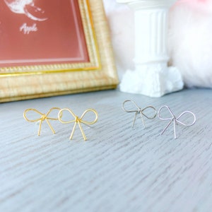 May include: Two pairs of gold and silver bow-shaped earrings. The earrings are on a wooden surface.