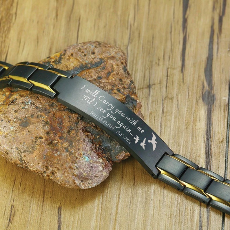 May include: Black and gold stainless steel bracelet with an engraved message: "I will Carry you with me 'Til I see you again... Dad | 12.22.1956-10.13.2022". The bracelet features a design of three flying birds.