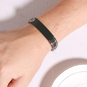 May include: A black and gold bracelet with a rectangular plate. The bracelet is made of metal and has a magnetic clasp.