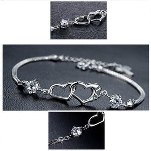 May include: Silver bracelet with two interlocking heart charms and clear cubic zirconia stones.