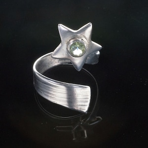 May include: A silver ring with a star-shaped design and a green gemstone in the center.