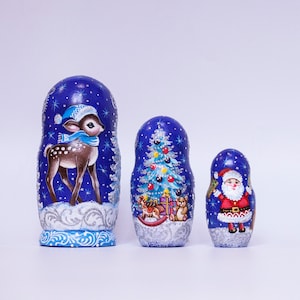 May include: A set of three blue and silver painted Russian nesting dolls, or matryoshka dolls, with winter holiday themes. The largest doll features a deer in a blue hat, the middle doll features a Christmas tree, and the smallest doll features Santa Claus.