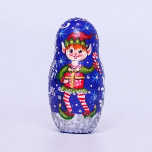 May include: A blue and silver Christmas-themed nesting doll with a painted image of an elf holding a gift and candy cane.