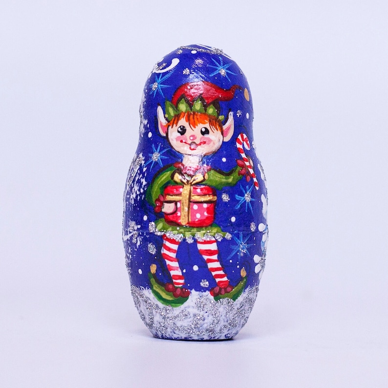 May include: A blue and silver Christmas-themed nesting doll with a painted image of an elf holding a gift and candy cane.