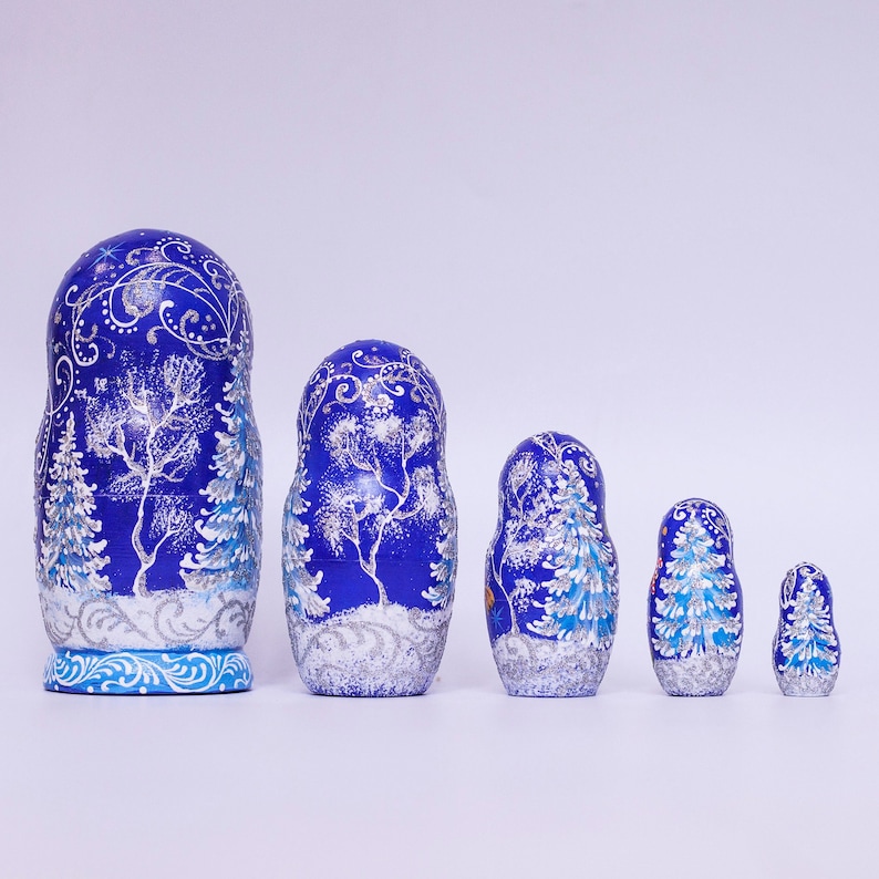 May include: A set of five blue and silver Russian nesting dolls, or matryoshka dolls, with a winter forest scene painted on them. The dolls are arranged in order of size, with the largest doll on the left and the smallest doll on the right.