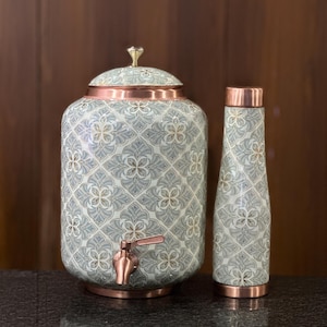 Könnte beinhalten: Ein zylindrischer Wasserspender mit Zapfhahn und eine passende hohe Flasche, beide mit einem hellgrauen und weißen Blumenmuster sowie kupferfarbenen Metallakzenten an Boden, Deckel und Auslauf, gekrönt von einem kleinen metallischen Knauf.