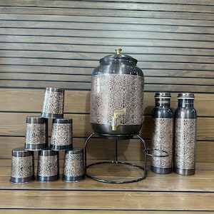May include: A decorative copper-colored drink dispenser set with matching cups and water bottles. The dispenser has a spigot and sits on a black metal stand. The cups and bottles are arranged around the dispenser.