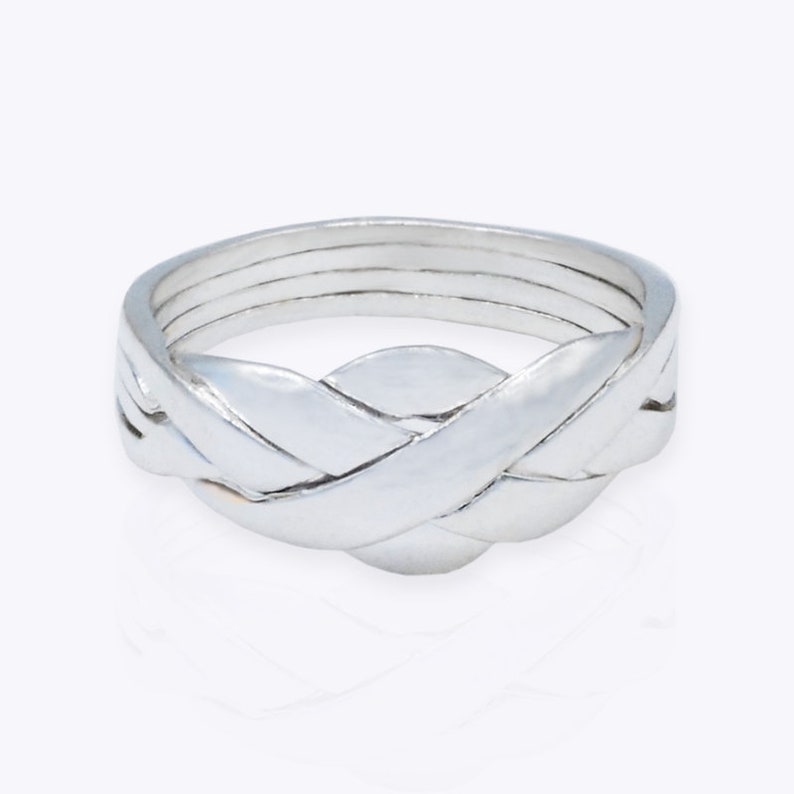 K&ouml;nnte beinhalten: Ein silberfarbener Puzzle-Ring bestehend aus vier ineinandergreifenden B&auml;ndern, die zusammen eine geschlossene Einheit bilden. Die Metalloberfl&auml;che ist glatt und reflektierend und zeigt ein komplexes, geflochtenes Design mit poliertem Finish.