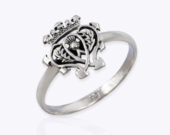 Könnte beinhalten: Ein silberner Ring mit einem detaillierten Design eines Herzens mit einer Krone und einem Distel darin. Der Ring befindet sich auf einem weißen Hintergrund.