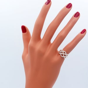 Könnte beinhalten: Ein silberner Ring mit einem geflochtenen Design. Der Ring befindet sich an einem Modellfinger.