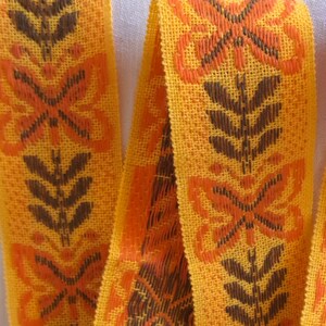 Jaren 1970 geweven diep oranje, geel en bruin linnen lint. Vlinders en bladeren. Mooie dikke kwaliteit: 5,5 cm breed. Sterke kleuren.