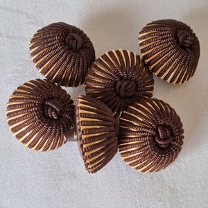 Pode incluir: Seis ornamentos decorativos de tecido castanho e dourado com textura canelada. Os ornamentos estão dispostos em um grupo.