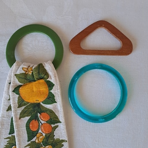 May include: Three different colored rings, one green, one brown, and one blue. The green ring is attached to a white tea towel with a lemon pattern.