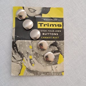 Puede incluir: Un paquete de cinco botones plateados para cubrir. El paquete está etiquetado con "Goodmans Trims Cover-Your-Own Buttons Cannot Rust".