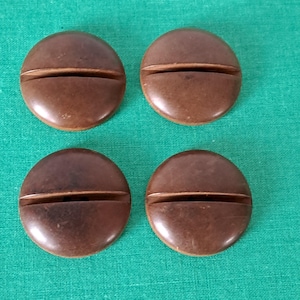 Pode incluir: Quatro botões de madeira castanho com uma ranhura no centro. Os botões são redondos e têm um acabamento brilhante.
