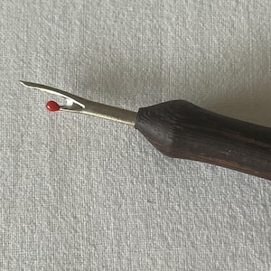 May include: A close-up of a seam ripper with a wooden handle. The seam ripper has a red tip and a metal blade.