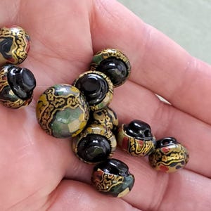 May include: A collection of ten decorative buttons with a black centre and a gold, green and red patterned design.