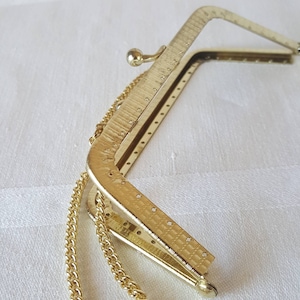 Kleine Bügeltasche. Vergoldeter Metallrahmen. Gebohrte Löcher für einfaches Befestigen am Stoff. Top Griff mit Kette. Kugelverschluss. Hergestellt in Schweden.