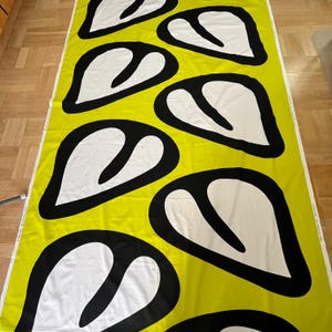 May include: Yellow fabric with a repeating pattern of black outlined white heart shapes.