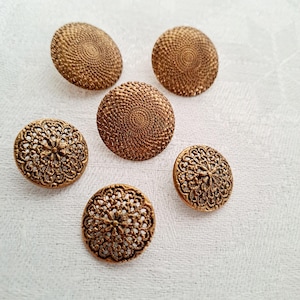 Puede incluir: Seis botones de metal de color dorado con diseños intrincados. Dos botones presentan un patrón circular, mientras que los otros cuatro tienen un diseño más delicado y de encaje.