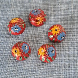Puede incluir: Cinco botones redondos rojos con un diseño floral. Los botones tienen flores amarillas, azules y verdes sobre un fondo rojo.