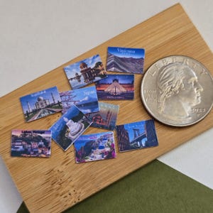 Peut inclure: Un ensemble de mini-cartes postales souvenirs représentant des monuments du monde entier, dont le Taj Mahal, la Tour Eiffel et le pont de Brooklyn. Une pièce de monnaie est incluse pour l'échelle. Les cartes sont disposées sur une surface en bois.