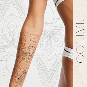 Peut inclure: Un tatouage en noir et blanc représentant un lotus, des croissants de lune et des motifs géométriques sur le bras d'une personne. Le tatouage est sur un fond blanc avec un motif de mandala gris.