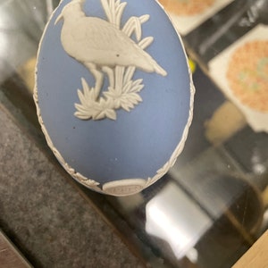 May include: A blue and white ceramic egg with a white bird design and the year 1983 on the bottom.
