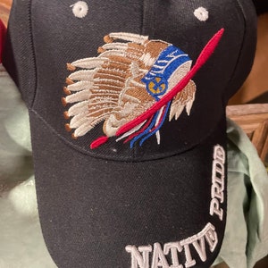 May include: Black baseball cap with an embroidered Native American headdress design in brown, red, blue, and white. The words "NATIVE" and "PROUD" are embroidered in white on the cap.