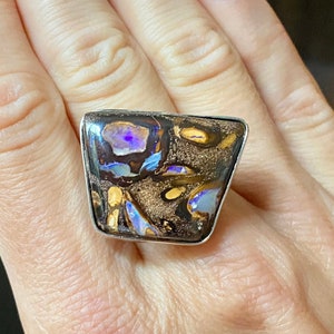 May include: A silver ring with a large, rectangular, multi-colored opal stone. The opal has a dark brown base with flashes of blue, purple, and gold.