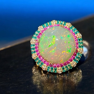 May include: A ring with a large, white opal gemstone surrounded by a halo of smaller pink and green gemstones.