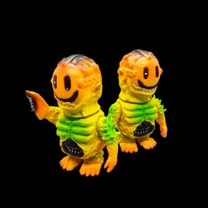May include: Two yellow and green monster figurines with smiling faces and exposed ribcages. The figures have a spiky, textured surface and are posed with their arms outstretched.