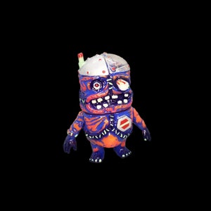 May include: A small, blue and orange, hand-painted, robot toy with a stitched-on, exposed, orange and purple, flesh-like body. The robot has a silver head with a clear plastic dome and a single, red, glowing eye.