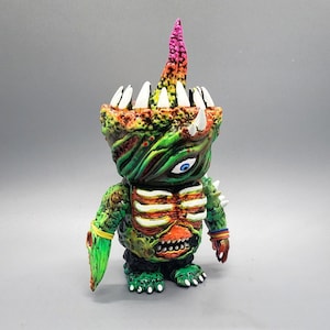 May include: A green, orange, and white monster toy with a rainbow-colored horn. The monster has a single large eye and a toothy grin. The toy is made of plastic and has a textured surface.
