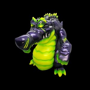 May include: A green and purple alligator figurine with a toothy grin. The figurine has a textured, scaly surface and is posed in a standing position.