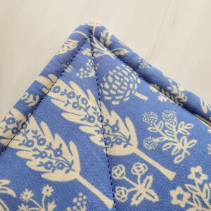 May include: Close-up of a blue fabric with a white floral pattern. The fabric is sewn with a straight stitch along the edge.
