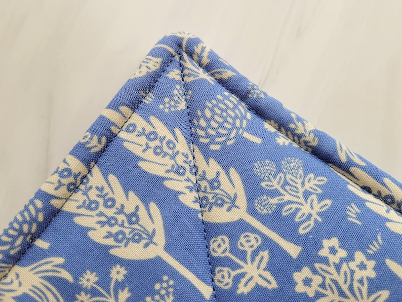 May include: Close-up of a blue fabric with a white floral pattern. The fabric is sewn with a straight stitch along the edge.