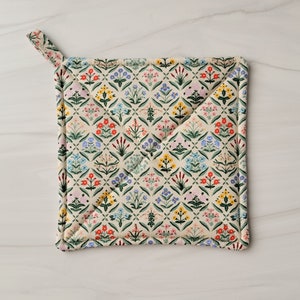 May include: A cream-colored quilted hot pad with a floral pattern in shades of pink, blue, yellow, and green. The pattern features a repeating design of small flowers and leaves.