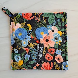 May include: A black quilted hot pad with a floral pattern featuring pink, blue, yellow, and red flowers on a black background. The hot pad has a loop handle.