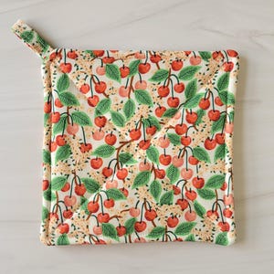 May include: A white quilted hot pad with a cherry print. The cherries are red with green stems and leaves. The hot pad has a loop handle.