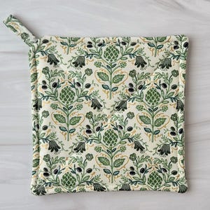 May include: Square pot holder with a loop for hanging. The cream-colored fabric is patterned with green floral and leaf designs, with accents of black and gold. The pot holder is quilted for heat resistance.