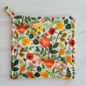 May include: A white cotton pot holder with a floral pattern featuring red, pink, yellow, and green flowers. The pot holder has a loop handle.