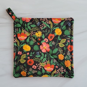 May include: A black pot holder with a floral pattern featuring red, pink, yellow, and green flowers on a dark background. The pot holder has a loop handle.