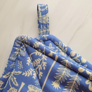 May include: A blue quilted pot holder with a white floral pattern and a hanging loop.