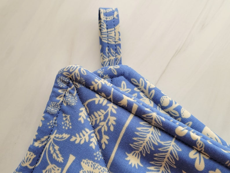 May include: A blue quilted pot holder with a white floral pattern and a hanging loop.