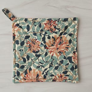 May include: Square floral pot holder with a loop for hanging. The fabric features a cream background with a pattern of orange, teal, and navy flowers and leaves. The pot holder is approximately 8 inches square.