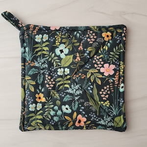 May include: A dark green quilted hot pad with a floral pattern featuring pink, yellow, and blue flowers. The hot pad has a loop handle.