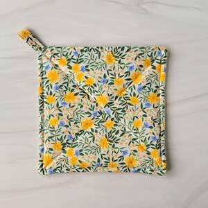May include: A white quilted hot pad with a floral pattern featuring yellow and blue flowers on green stems.
