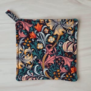 May include: Square floral pot holder with a loop for hanging. The fabric features a dark navy background with a pattern of orange, pink, yellow, and white flowers and foliage. The edges are trimmed in a teal color.
