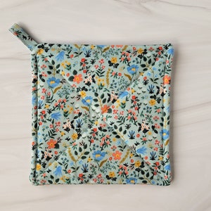 May include: A light blue quilted hot pad with a floral pattern. The pattern features small blue, pink, yellow, and orange flowers on a light green background.